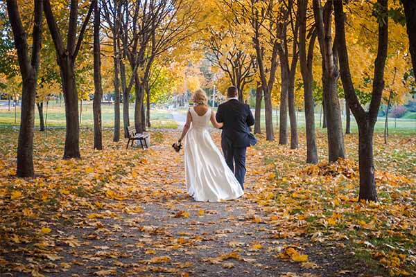 bruidspaar dat tussen de herfstbomen loopt